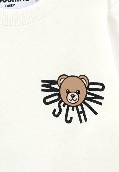 Felpa bianca con grafica di un orso in stile cartone animato con un volto marrone e il testo "Moschino" in bold nero, che presenta un design giocoso.
