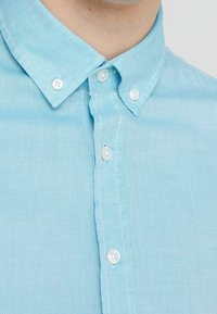 Jasnoniebieska koszula na guziki z teksturowanej tkaniny, z klasycznym kołnierzykiem i białymi plastikowymi guzikami z przodu.