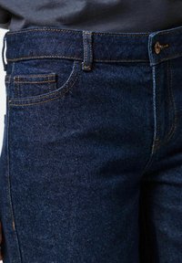 Denim jeans made of dark blue fabric with contrasting orange stitching, featuring a front pocket, belt loops, and a metal button closure.