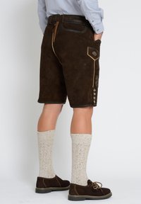 Ruske sueded hlače s bočnim džepovima, vezom naglašenim detaljima i kontrastnim bež šavovima. U kombinaciji s krem čarapama do koljena i smešnim cipelama.