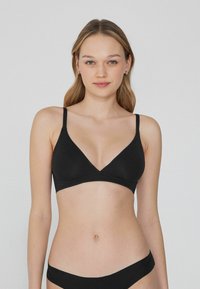 Bralette triangle noir avec de fines bretelles réglables, tissu lisse et décolleté en V. Design sans couture pour une esthétique minimaliste.