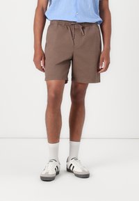 Shorts en coton marron avec une taille élastique et un cordon de serrage, poches latérales et coupe décontractée, associés à des baskets blanches et des chaussettes.