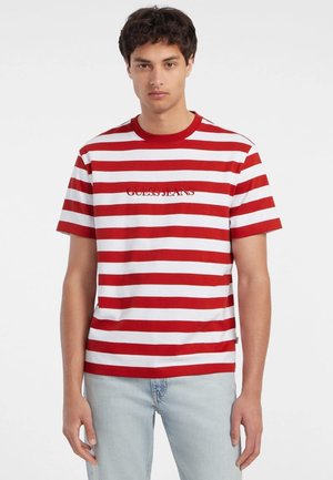 Raudonai ir baltai dryžuota marškinėliai su apvalia iškirpte ir trumpomis rankovėmis; ant krūtinės yra užrašas "GUESS JEANS".