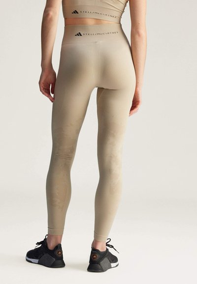 Leggings beige con un motivo testurizzato, vita alta e dettaglio del logo sulla parte posteriore. Abbinati a scarpe da ginnastica nere.
