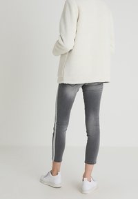 Crème fleece jack met lange mouwen, gecombineerd met slim-fit grijze jeans met een witte zijstreep en witte sneakers.
