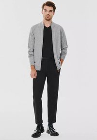 Szara bomberka zapinana na zamek, noszona na czarnej koszulce, w zestawieniu z czarnymi spodniami i czarnymi butami. Gładkie faktury, dopasowany krój.