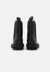 Botas de tobillo de cuero negro con un acabado texturizado, paneles laterales elásticos y una suela de goma gruesa. Lengüeta en la parte posterior para facilitar su uso.