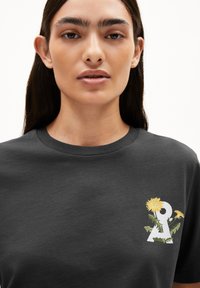 Schwarzes Baumwoll-T-Shirt mit weißem gesticktem Buchstaben "A" und gelben Löwenzahnblüten sowie grünen Blättern, Rundhalskragen, kurze Ärmel.