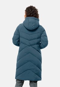 Lungo cappotto puffo teal con cappuccio, caratterizzato da un motivo a zigzag, texture trapuntata e una silhouette leggermente svasata in vita.