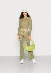 Conjunto de blusa de manga longa com padrão verde e calças largas, acompanhado de uma bolsa de mão verde clara à condizer. Modelo a usar sapatilhas brancas e um chapéu de balde claro.