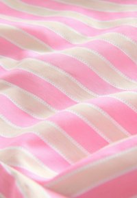 Tkanina bawełniana w naprzemienne faliste różowe i kremowe paski, ozdobiona delikatnym białym przeszyciem na krawędziach. Gładka faktura.