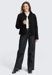 Czarna pikowana kurtka zapinana na zatrzaski na białym golfie, zestawiona z ciemnymi, wysokim stanem jeansami i czarnymi butami.