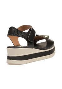 Sandalia de cuña negra de cuero con correa ajustable, parte superior texturizada y una suela de plataforma blanca y negra. Presenta un detalle metálico en la correa.