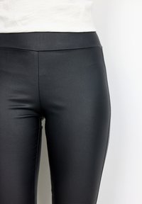 Leggings in ecopelle nera con una texture liscia, vita alta e design aderente, mostrati su uno sfondo neutro.