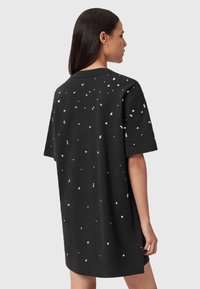 Donna di spalle che indossa un abito t-shirt nero oversize con piccole decorazioni bianche sparse sulla schiena e sulle maniche.