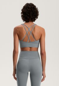 Siv bras za šport z prečnimi naramnicami in gladko teksturo, v kombinaciji z visokimi pajkicami iste barve in materiala.