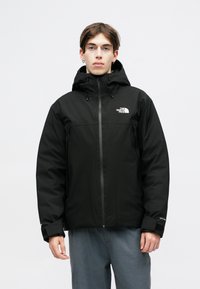 Čierna izolačná bunda s kapucňou, vybavená predným zipsom, nastaviteľnými manžetami a logom The North Face na hornej ľavej časti hrude.