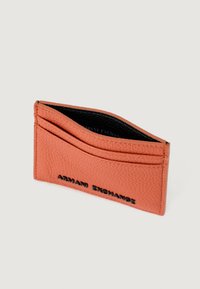 Tarjetero de cuero texturizado naranja con el logo negro de "Armani Exchange" y múltiples ranuras para tarjetas sobre un fondo claro.