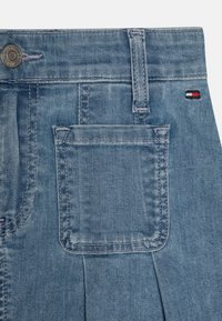 Light blue denim shorts featuring a front button, a back pocket, and contrasting stitching details. Tommy Hilfiger logo in red, white, and blue.