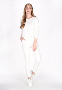 Hvid langærmet cropped top med rund halsudskæring, parret med tætsiddende hvide bukser og hvide sneakers. Glat stof, enkelt design.