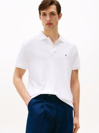 Witte polo met een kraag en korte mouwen, gecombineerd met marineblauwe broek. Heeft een klein logo op de linkerkant van de borst.
