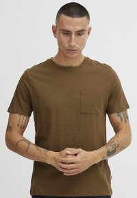 Brun kortermet t-skjorte laget av myk stoff, med brystlomme og subtil tekstur. Ledig passform med rund hals.
