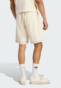 Kreminės spalvos šortai su elastine juostele, puošti kontrastingais siuvinėjimais. Dėvimi su baltais kojiniais ir kreminėmis sportbačiais.