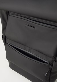 Black backpack made of smooth nylon with multiple zippered pockets, featuring embossed logo and sleek design. Minimalistic structure and texture.