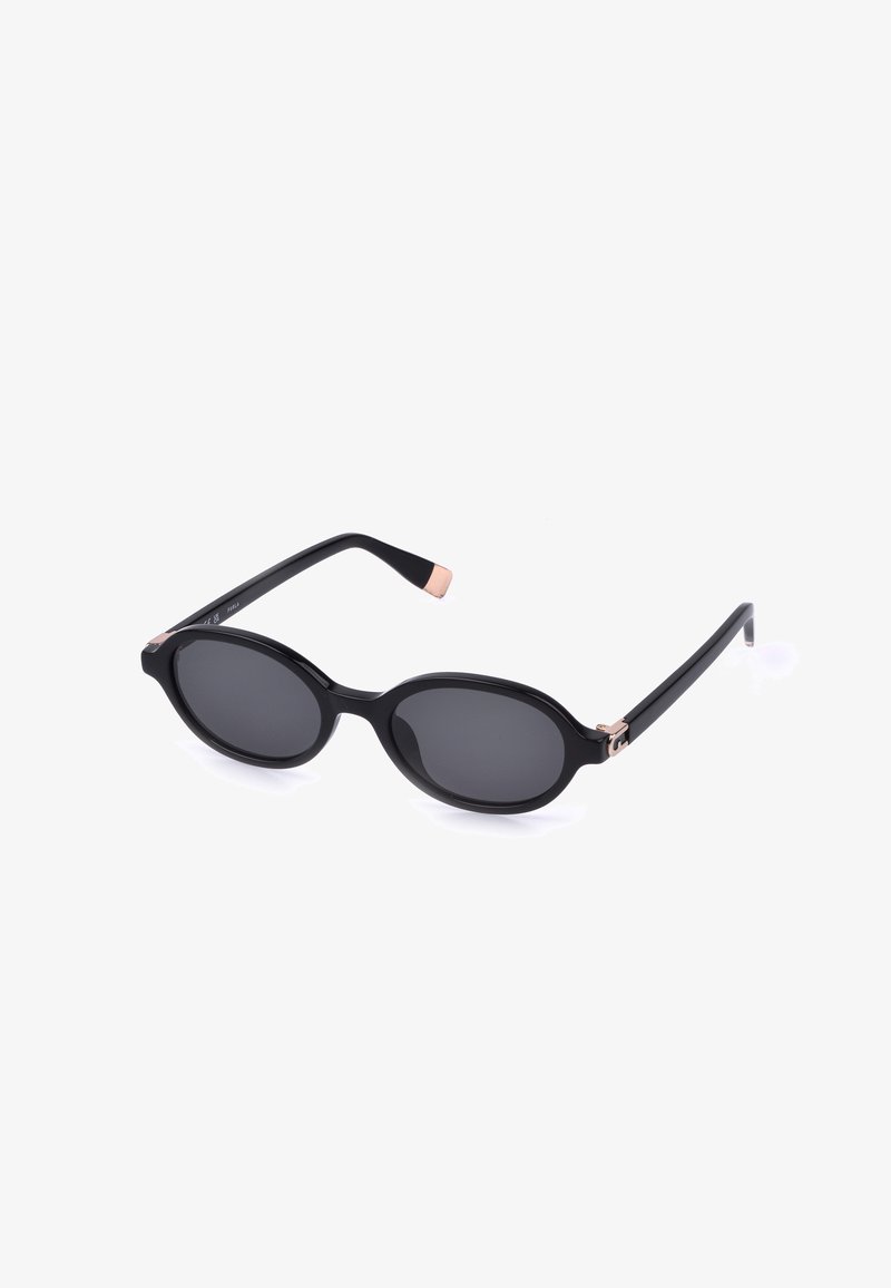 Lunettes de soleil ovales noires avec des verres foncés, des branches fines et de petits accents en or rose aux charnières et aux bouts des branches.