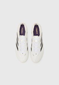 Witte voetbalschoenen met zwarte strepen, gestructureerde bovenkant, witte veters, paarse binnenzolen en gouden "COPA" branding op de tong.