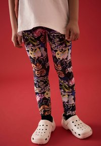Leggings colorati con un motivo grafico misto in diverse tonalità, abbinati a scarpe bianche senza lacci con fori di ventilazione.