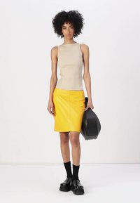 Beige žebrovaný top bez rukávů v kombinaci se žlutou koženou tužkovou sukní. Černé robustní boty a černá taška celý outfit završují.