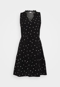 Robe noire sans manches à pois blancs, encolure en V, bordure froncée et jupe à volants. Fabriquée en tissu léger.