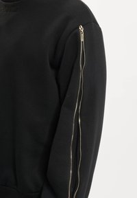 Čierna mikina so štandardným výstrihom a priliehavým strihom. Má zlatý zips na ľavom rukáve pre jedinečný detail.