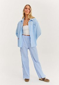 Světle modrá oversize košile, pruhované modro-bílé kalhoty a boty se zvířecím vzorem. Obsahuje bílý crop top a vrstvené náhrdelníky.