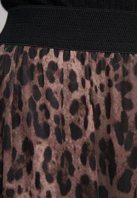 Zwart elastische tailleband boven een doorschijnende roze stoffen rok met een transparante luipaardprint in donkerbruin en zwart.
