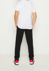 Witte katoenen T-shirt met korte mouwen, gecombineerd met zwarte broek. De outfit wordt compleet gemaakt met rode en zwarte sportschoenen.