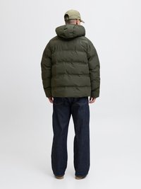 Kurtka puchowa w ciemnozielonym kolorze, z kapturem, pikowaną teksturą i luźnym krojem. Zestawiona z luźnymi, ciemnoniebieskimi dżinsami i pasującą czapką.