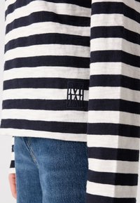 Langermet stripete skjorte i marineblått og hvitt bomull, med en brodert logo-lapp på kanten, kombinert med blå denimjeans.