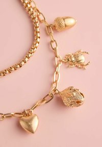 Zelta tonis ķēde ar piekariņiem: zīle, vabole, sirds un sīki izstrādāta vardes figūra, ar dažādām tekstūrām un spīdīgām apdarēm.