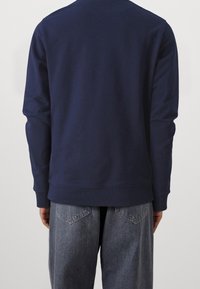 Felpa blu navy con maniche lunghe, polsini e orlo a costine, indossata sopra jeans grigio chiaro dalla vestibilità ampia con tasche posteriori.