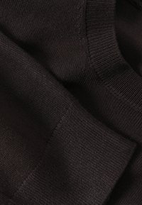Gros plan sur un tissu tricoté marron foncé montrant les textures côtelées détaillées du col et des poignets.