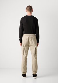 Beige cargo-housut, joissa on elastiset hihnat ja kaksi sivutaskua. Päällä musta pitkähihainen paita, katsottuna takaa. Sileä pinta.