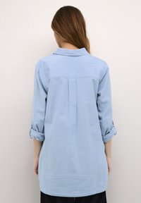 Camicia azzurro chiaro con bottoni e maniche lunghe arrotolate ai polsi, con yoke posteriore e piega, realizzata in un tessuto liscio.