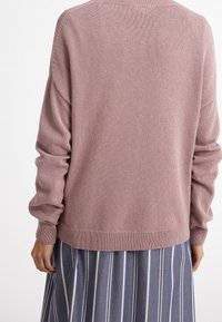 Pull tricoté rose clair à coupe décontractée, avec poignets et ourlet côtelés. Le dos présente un motif texturé, associé à une jupe rayée.