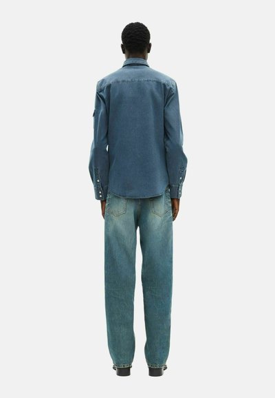 Camicetta in denim con lavaggio medio, maniche lunghe e polsini a bottone, abbinata a jeans a gamba larga di colore blu chiaro, dotati di tasche classiche e cuciture.