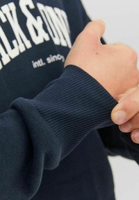 Sudadera en color marino con puños acanalados y texto impreso en blanco en el pecho. La textura de la tela parece suave y ligeramente elástica.