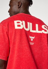 Rød bomulds T-shirt med en falmet finish, der har stort hvidt "BULLS" tekst og et Chicago Bulls-logo på ryggen. Korte ærmer.
