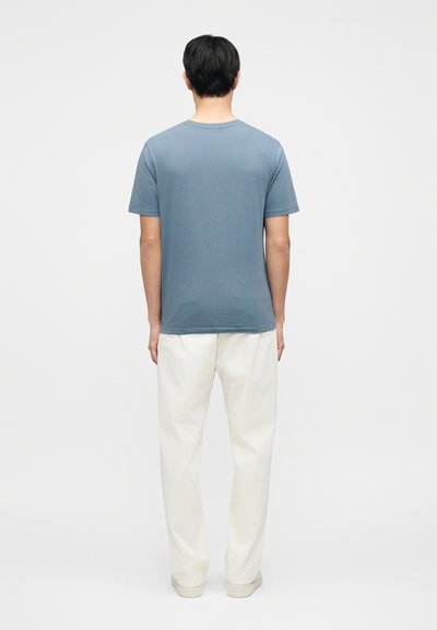 T-shirt gris avec un col rond, des manches courtes et une coupe décontractée, associé à un pantalon ample de couleur blanc cassé.