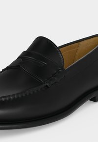Mocassin homme en cuir noir avec bout mocassin, détail de bride penny et doublure intérieure marron clair.